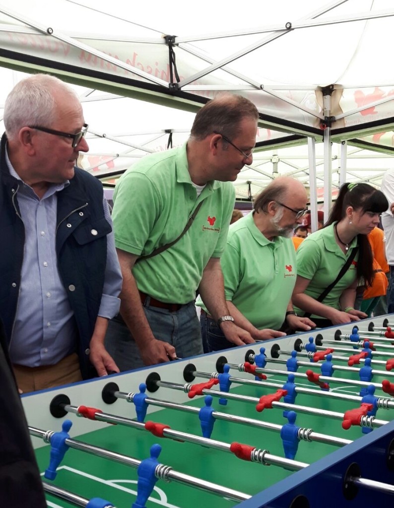 Mehrere Personen stehen hinter einem Tischkicker, konzentriert beim Spielen, während die Atmosphäre unter Zelten attraktiv ist.