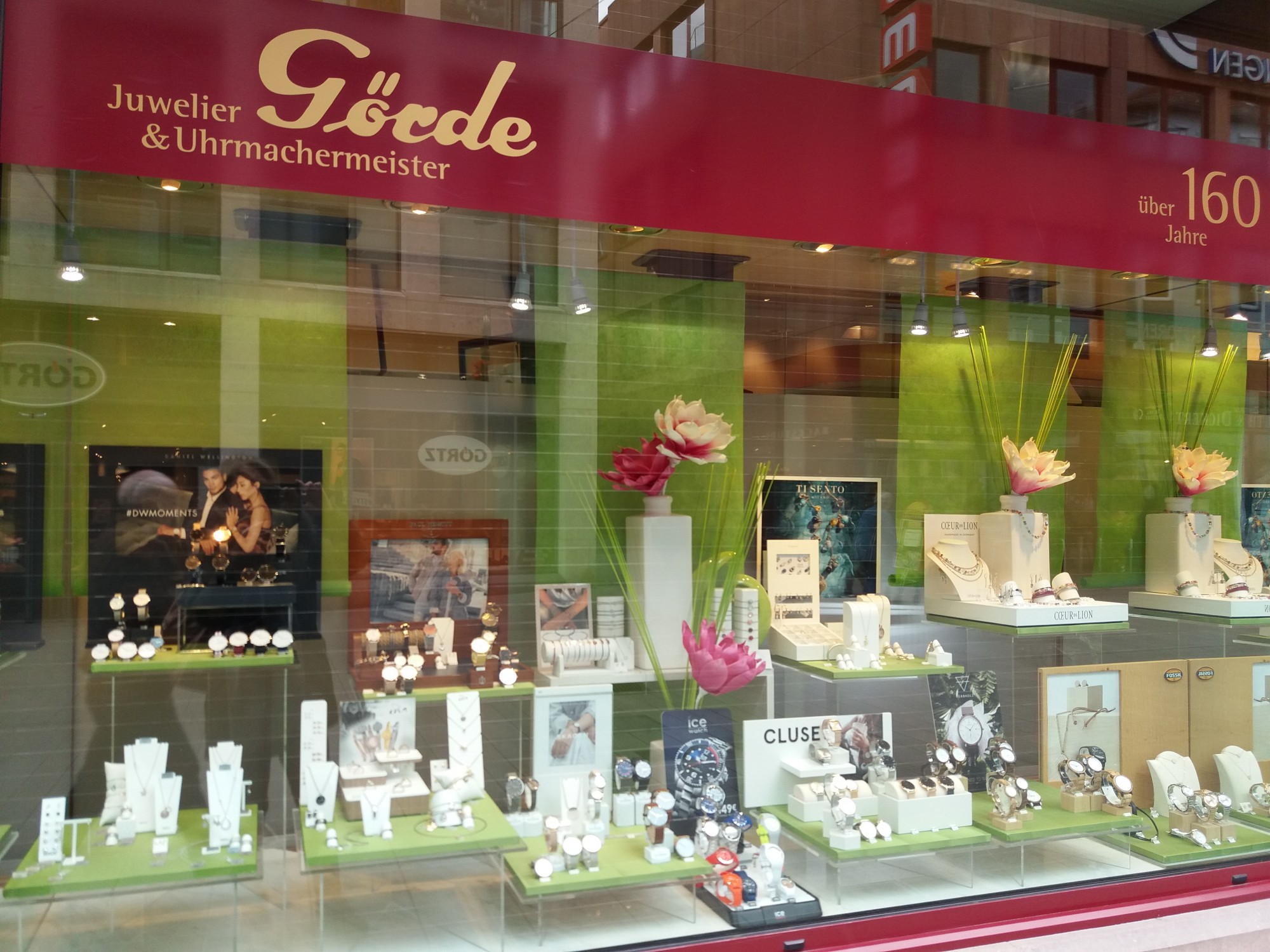 Das Schaufenster eines Juweliergeschäfts zeigt eine Vielzahl von Schmuckstücken und Uhren auf grünen Unterlagen. Über dem Fenster prangt der Schriftzug 