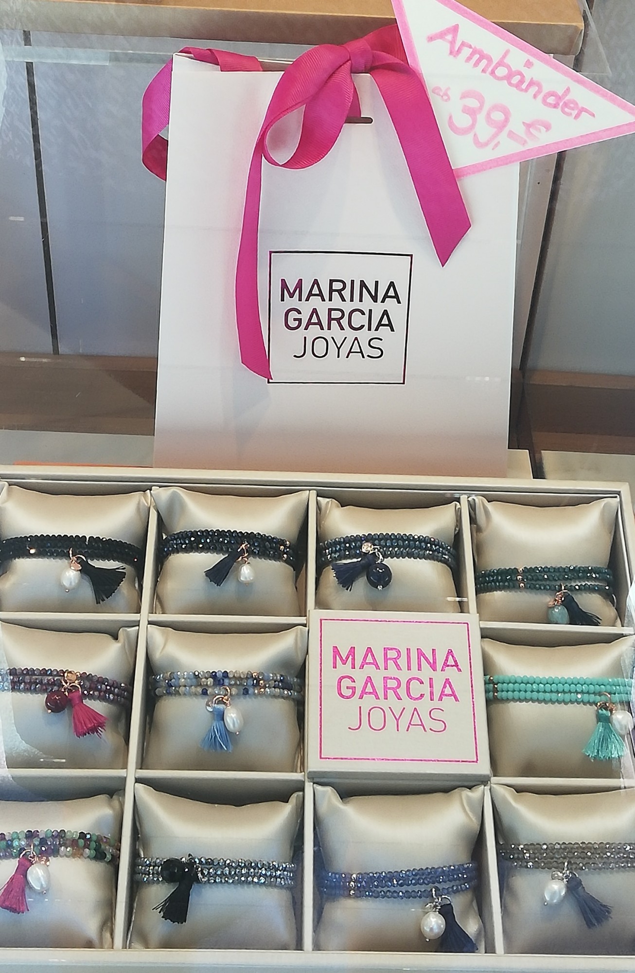 Eine elegante Schmuckauslage mit verschiedenen Armbändern, die auf Kissen präsentiert werden. Im Hintergrund eine Einkaufstasche mit dem Logo 