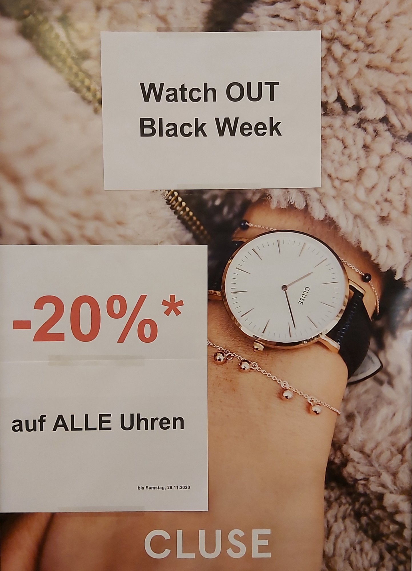 Ein Werbebild zeigt eine elegante Armbanduhr auf einem Handgelenk, umgeben von Schmuck. Darauf sind Angebote für die Black Week und Preisnachlässe zu sehen.