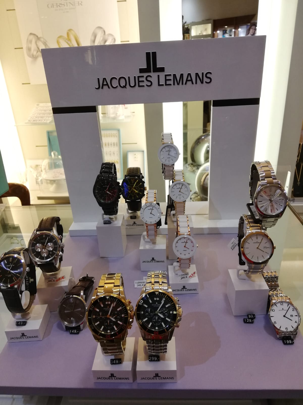 In einem Schaufenster sind mehrere Uhren der Marke Jacques Lemans in verschiedenen Designs und Farben ausgestellt.