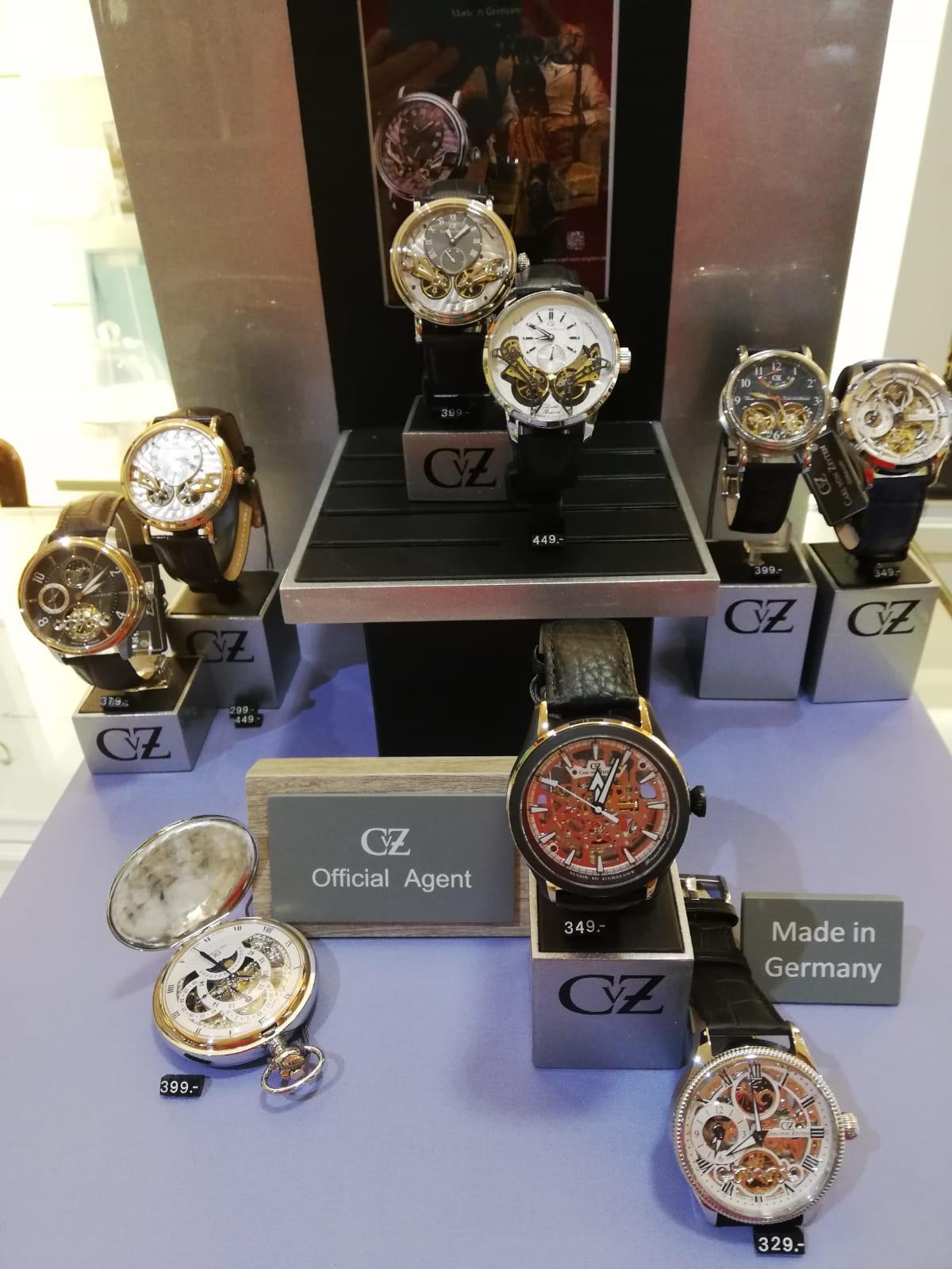 Das Bild zeigt eine Auswahl von Uhren in einem Schaufenster, einschließlich Armbanduhren und einer Taschenuhr, mit Preisschildern.