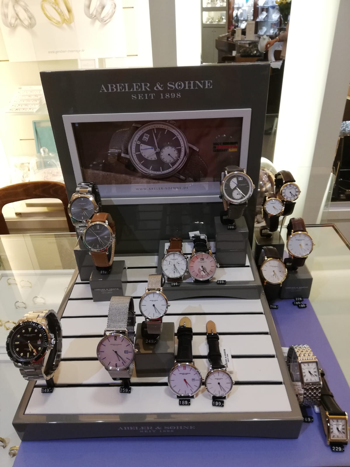 Ein Verkaufsständer mit mehreren Uhren der Marke Abeler & Söhne. Im Hintergrund ein großes Bild einer Armbanduhr und Preisschilder aufgestellt.