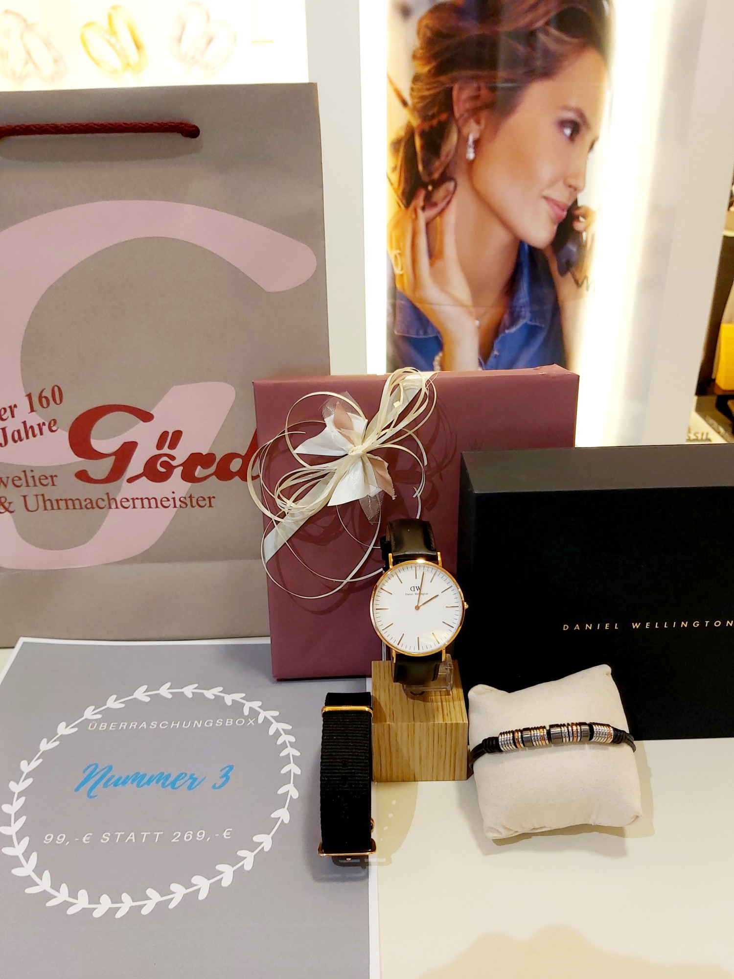 Ein Schmuckgeschäftsdisplay mit einer Uhr, einem Armband, Geschenkboxen, einer Einkaufstasche und einer Werbeanzeige für Überraschungsboxen.