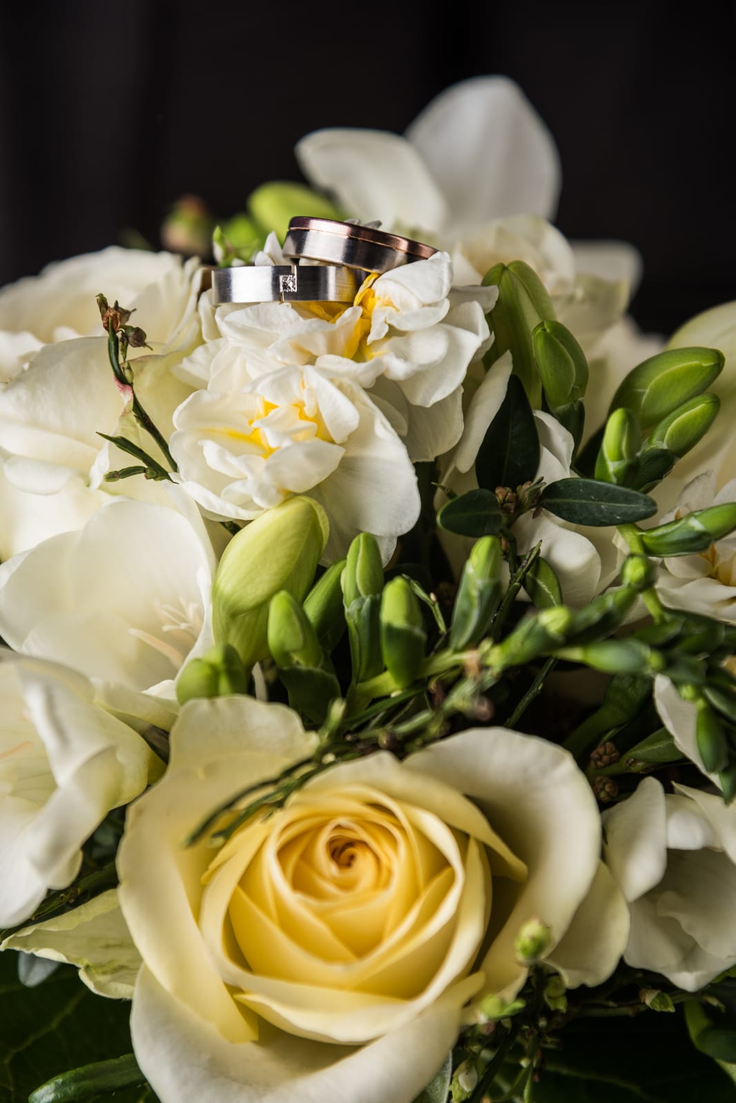 Ein schöner Blumenstrauß mit weißen und gelben Blumen, in dessen Mitte zwei Eheringe liegen, die elegant auf den Blüten platziert sind.