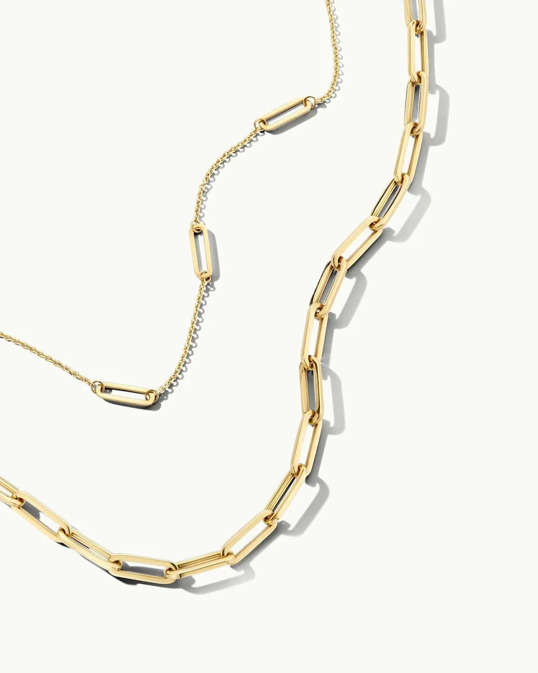 Eine elegante goldene Halskette mit flachen, rechteckigen Gliedern, die auf einem hellen Hintergrund platziert ist. Schatten werfen ein schönes Spiel mit Licht.