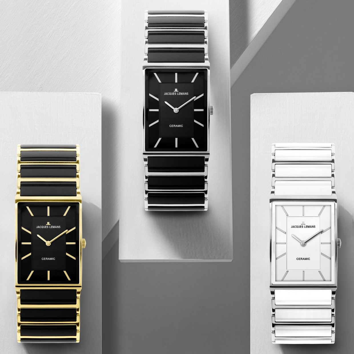 Drei elegante Uhren in modernem Design stehen auf weißen Podesten. Die linke Uhr hat ein schwarzes Ziffernblatt mit goldfarbener Auflage, die mittlere ein ähnliches schwarzes Ziffernblatt, während die rechte Uhr ein weißes Ziffernblatt aufweist.