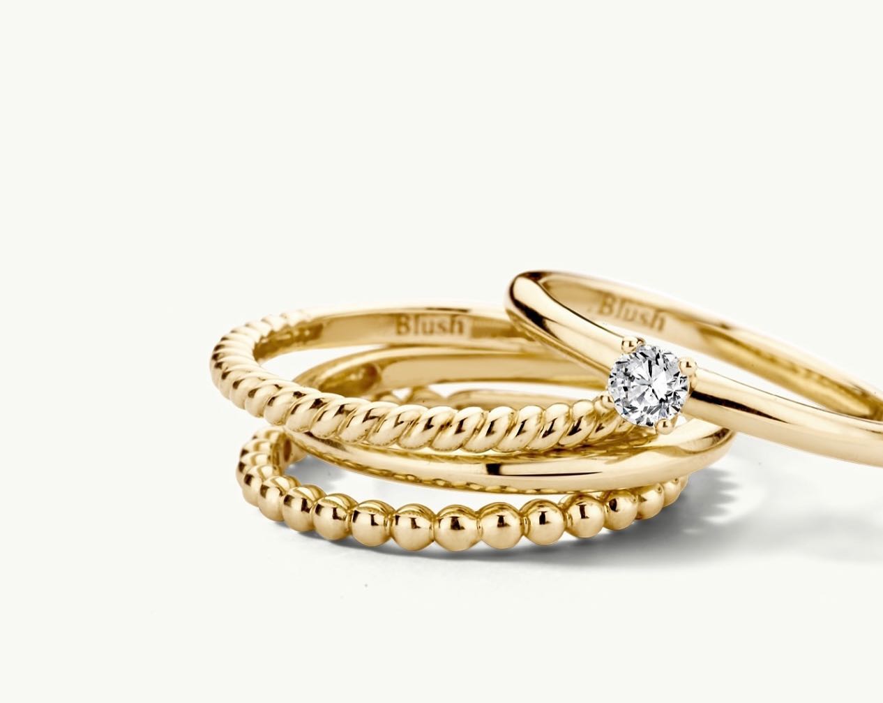 Drei goldene Ringe liegen nebeneinander auf einem hellen Hintergrund. Ein Ring hat eine gedrehte Struktur, ein anderer ist mit Kügelchen verziert, und der dritte hat einen strahlenden Diamanten.