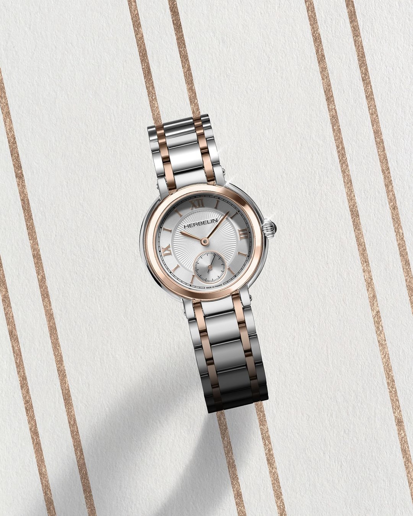 Eine elegante Herrenuhr mit silbernem und roségoldenem Armband liegt auf einer strukturierten, hellen Oberfläche mit feinen, goldenen Streifen.